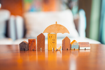 Wooden houses in a row with umbrella above, symbolizing home insurance, real estate protection,...