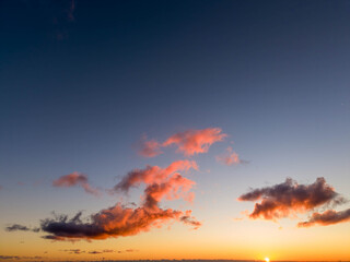 sunset scene with the sun touching the horizon and pink-tinged clouds drifting across a deepening blue sky in a peaceful atmosphere
