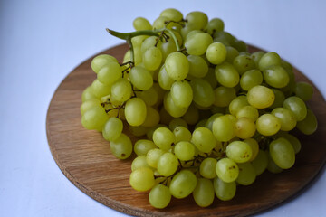 Large bunch yellow grapes on wooden plate. Food and summer background. Ripe grape Kishmish, sultana on wooden circle surface.