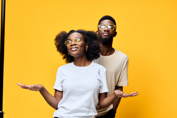 Smiling young couple with glasses against a vibrant yellow background, representing joy and positivity with a modern, stylish look