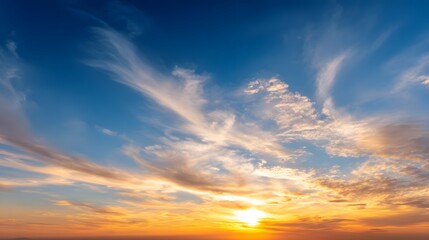Obraz premium Vibrant golden hour sun illuminates high wispy clouds against a deep blue expanse.