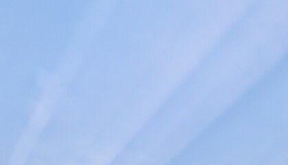 Subtle crepuscular sun rays stretch diagonally across a soft, pale blue sky, creating a minimalist and serene atmospheric background with maximum copy space.