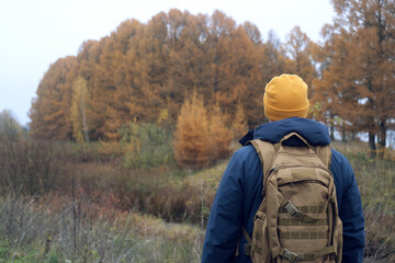 Man in the yellow hat hiking through autumn forest landscape with backpack