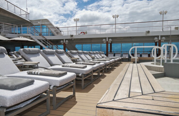 Guest pooldeck or swimmingpool with sun deck on modern family cruiseship or cruise ship liner with elegant lounge furniture deck chairs and rattan sun beds loungers