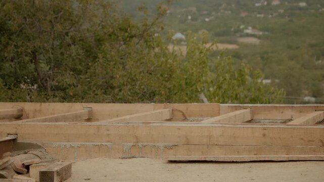 Wooden formwork holds the wet concrete in place as it dries, showing the progress of house construction amid a scenic outdoor location.