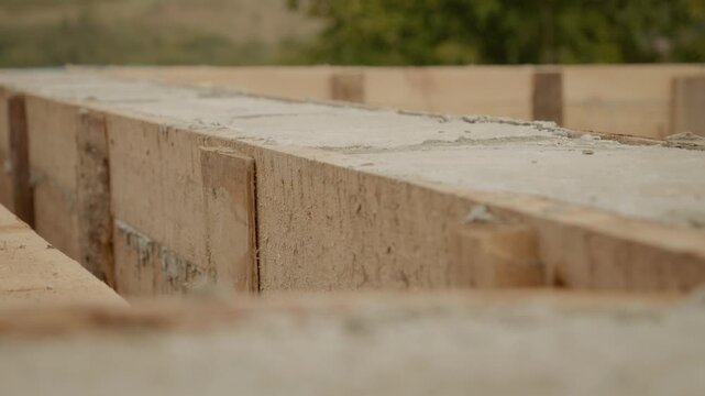 Wooden formwork is being used as concrete dries in a house construction site. Workers prepare the structure while ensuring the material sets properly for durability.