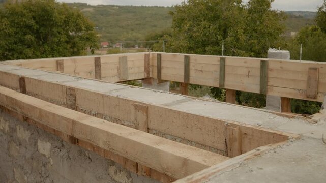 This shows the concrete drying process within wooden formwork during house construction. Workers prepare the structure in a serene location surrounded by nature.
