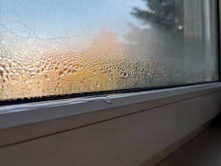 Close-up photo of condensation and water droplets on window glass in cold weather with blurred autumn landscape in the background. Great for weather, home comfort, or seasonal mood imagery