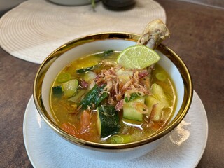 Hot bowl of homemade chicken soup with vegetables, lime, and herbs served in a rustic bowl. Ideal...
