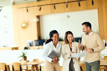 Three Colleagues Laughing and Reviewing Documents in Bright Modern Office