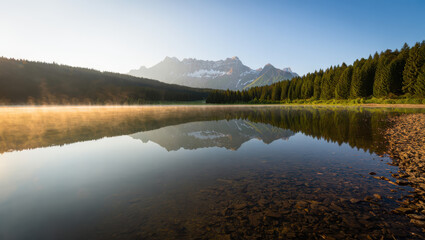 A serene lake reflecting mountains and trees under a clear blue sky at early morning light