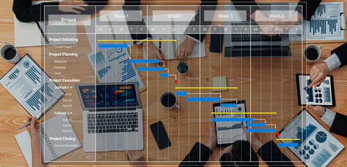 Aerial view of a diverse project management team collaborating on a presentation, including Gantt charts and data analysis in a modern office setting filled with tools and resources. Amity