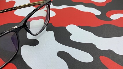 Eye catching eyeglasses with black frames laying on a red, white and black camouflage pattern