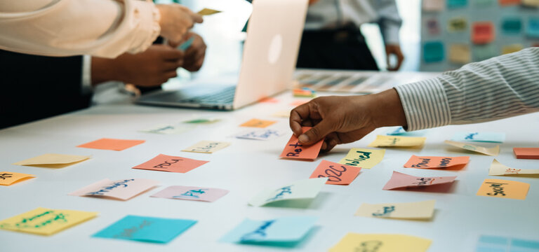 A dynamic office scene showcasing a team engaged in collaborative brainstorming using colorful sticky notes on a table, with a laptop in the background. SACTR
