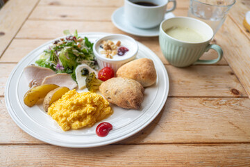 Healthy breakfast plate with scrambled eggs salad bread and coffee on wooden table