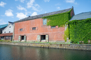 Old brick warehouse covered with ivy by canal on a sunny day at Hokkaido, Japan
