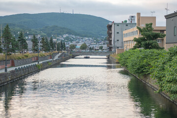 Calm river flowing through city with mountains in the background at Hokkaido, Japan