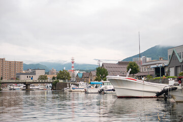 Fishing boats docked in harbor with city and mountains in background at Hokkaido, Japan