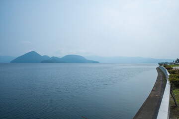Calm lake with distant mountains and curved shoreline under clear sky at Lake Toya, Abuta, Hokkaido, Japan