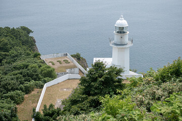 White lighthouse on green cliff overlooking calm sea coastline at Cape Chikyu, Muroran, Hokkaido, Japan