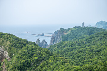 Lush green forested cliffs with lighthouse and ocean view on a hazy day at Cape Chikyu, Muroran, Hokkaido, Japan