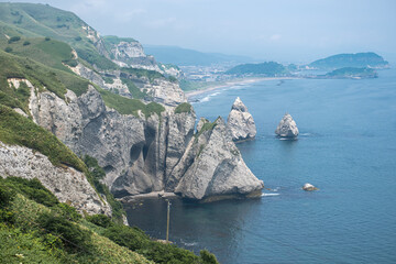 Rocky cliffs overlooking calm sea with distant coastline and hills at Cape Chikyu, Muroran, Hokkaido, Japan