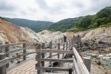 Tourists walking on wooden boardwalk in volcanic geothermal area with mountains at Noboribetsu Jigokudani Valley, Noboribetsu, Hokkaido, Japan