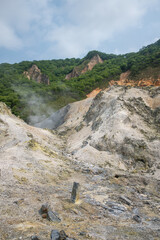 Volcanic landscape with steam vents and rocky terrain near forested hills at Noboribetsu Jigokudani Valley, Noboribetsu, Hokkaido, Japan