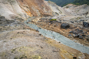 Geothermal hot spring stream flowing through rocky volcanic landscape at Noboribetsu Jigokudani Valley, Noboribetsu, Hokkaido, Japan