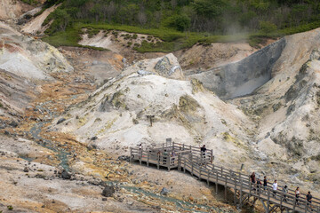 Tourists walking on wooden bridge in volcanic geothermal area with steam vents at Noboribetsu Jigokudani Valley, Noboribetsu, Hokkaido, Japan
