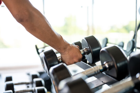 Close up of man client or fitness trainer coach's hand holding taking dumbbell to exercising in gym