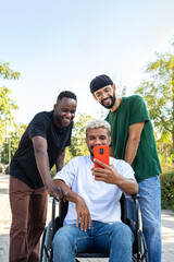 Vertical portrait of African American man in a wheelchair using phone together with male friends...