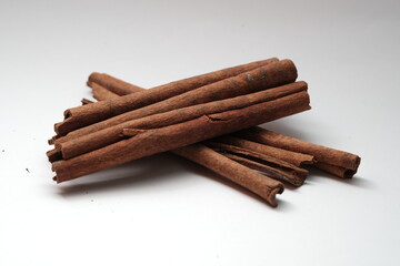 A small pile of dried cinnamon sticks arranged neatly on a clean white surface, commonly used for cooking, baking, and drinks.
