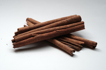 A small pile of dried cinnamon sticks arranged neatly on a clean white surface, commonly used for cooking, baking, and drinks.
