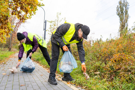 People Collecting Trash Along Roadside Volunteer Project in autumn park. Man and woman collect trash in bags outdoors. Save nature concept. Ecology care