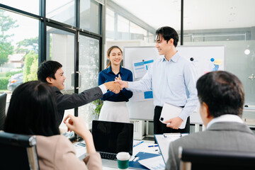Smiling Asian business team shaking hands after successful meeting, symbolizing partnership,...