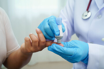 Asian woman self testing to check blood sugar level diabetes by digital lancet on finger at home.