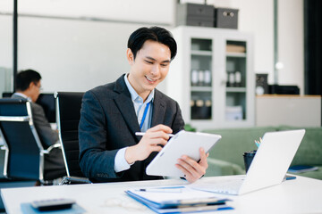 Confident Asian businessman using tablet and laptop in bright modern office, representing digital work, innovation