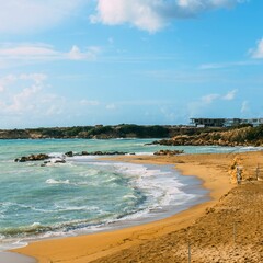 Sandy beach with gentle waves and distant buildings under a blue sky