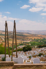 Close-up view of Fes hillside cemetery with scattered white tombs among rugged terrain under warm Moroccan light.