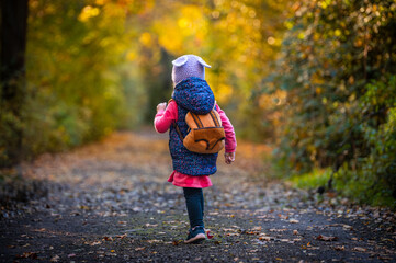 Adorable little girl with cute backpack playing in colorful autumn forest — warm fall tones, active childhood concept, copy space