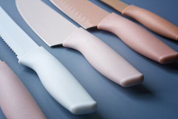 Close-up of modern pastel kitchen knives with silicone handles and color blades on a blue‑gray...