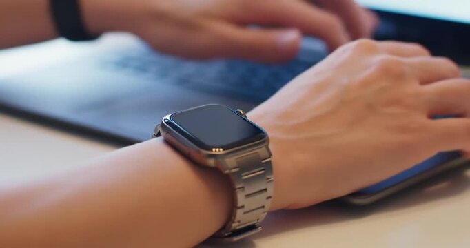 Person wearing a smartwatch while using a laptop computer. - Powered by Adobe