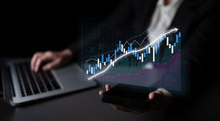 A businessman sits in a dark office with a laptop and smartphone, analyzing stock market data. The vivid digital graphs illustrate current financial trends and growth potential. Impute