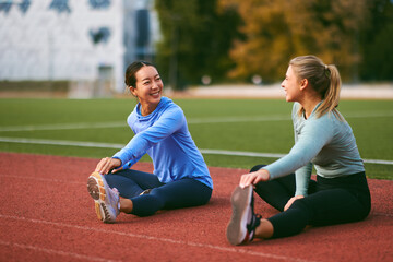 Women friends stretching on running track together