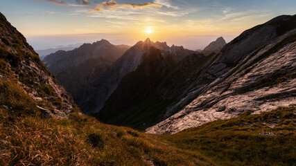 View of the sun cresting over jagged peaks, casting long shadows and highlighting the rugged terrain in golden light, Carrara, Tuscany, Italy.