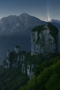 View of a comet blazing over the rugged mountains and ancient, moss-covered ruins, standing sentinel above the green landscape, Carrara, Tuscany, Italy.