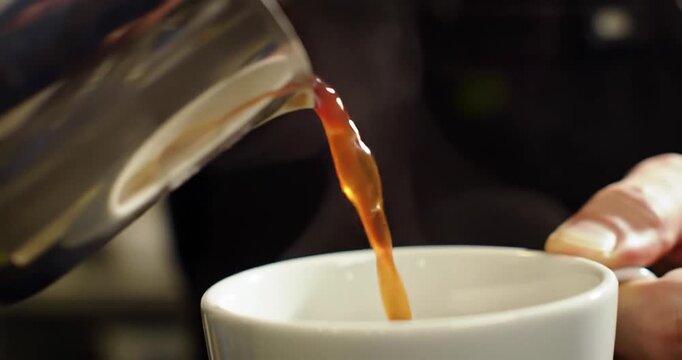 Pouring coffee into a white cup from a metal pitcher.