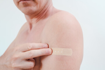 Close-up of a man's shoulder with adhesive bandage after vaccination or injection