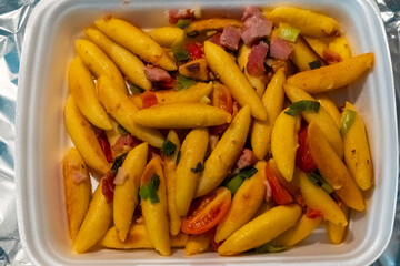 Delicious yellow pasta dish with vegetables and ham, served warm in a white container during a cozy evening meal